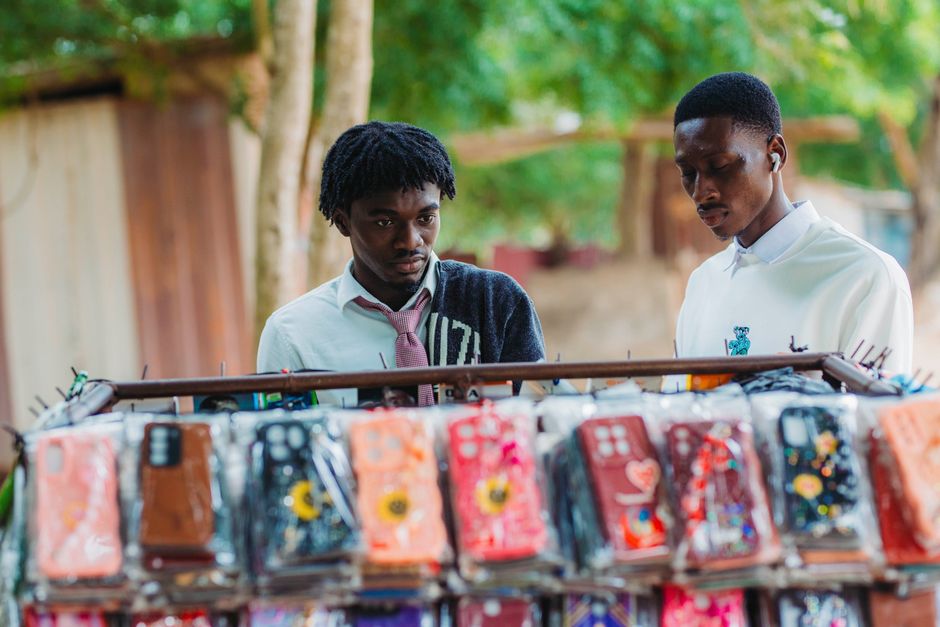 Young men exploring vibrant phone cases at a street market in Accra.