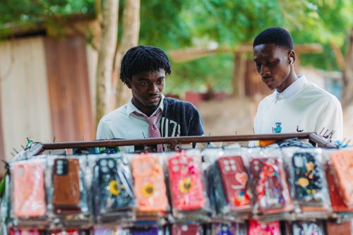 Free Young men exploring vibrant phone cases at a street market in Accra. Stock Photo