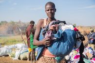 African woman holding a bundle of clothes outdoors, with people in the background, under a clear sky.