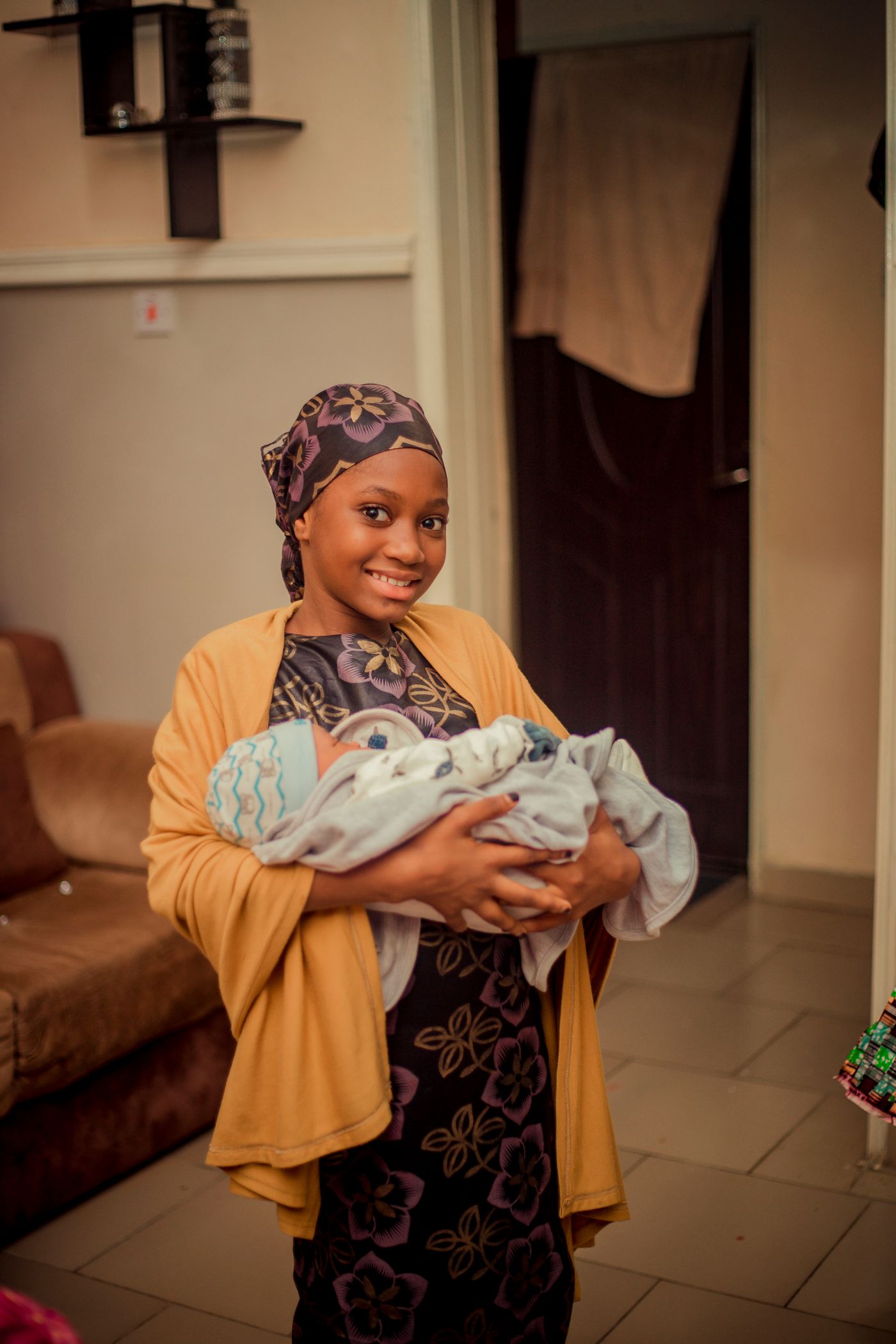 Smiling mother holding a small baby indoors while looking toward the camera