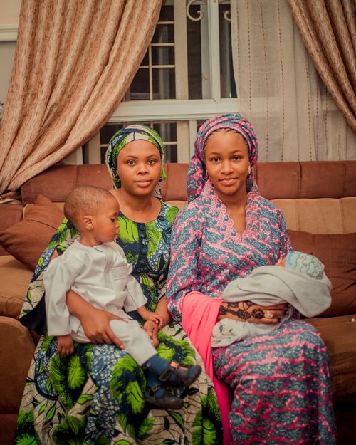 Free Two women and two children in colorful African attire sitting indoors, conveying warmth and tradition. Stock Photo
