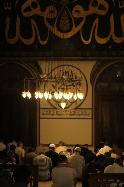 Free Worshippers engaged in prayer inside a historic mosque under ornate chandeliers. Stock Photo