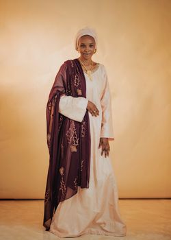 Graceful woman in traditional dress with patterned shawl against warm background.