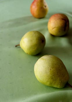 Four ripe pears placed on a soft green surface, capturing natural colors and textures.