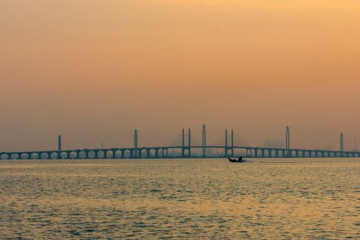 Scenic view of Penang Bridge at sunset with a fisherman boat on calm waters, Malaysia.