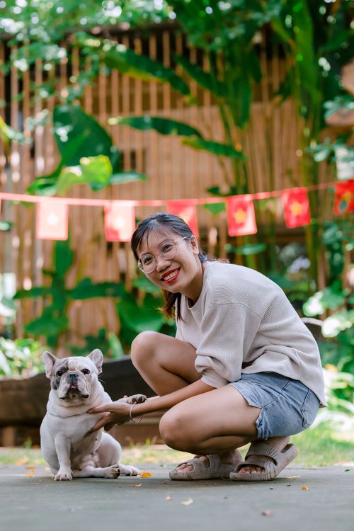 Free Happy woman crouching beside French Bulldog outdoors, enjoying a sunny day with festive decorations. Stock Photo