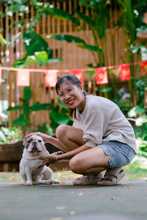 Free Smiling woman crouching next to a bulldog in a lush garden setting. Stock Photo