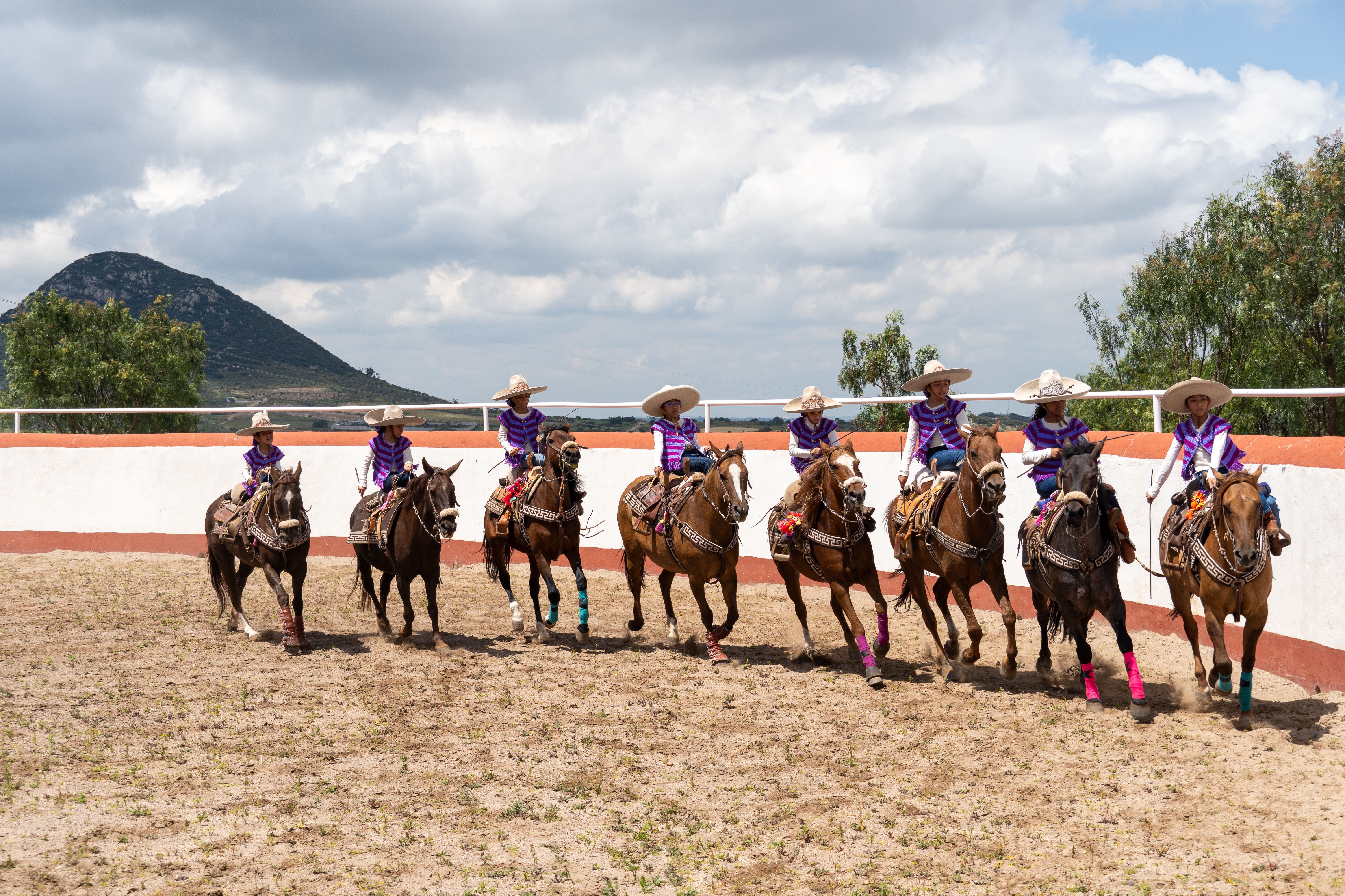 Colorful charro performance featuring riders on decorated horses in a Mexican arena.