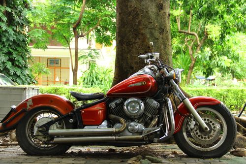 Free A classic red motorcycle is parked by a tree in an outdoor setting, showcasing vintage charm. Stock Photo