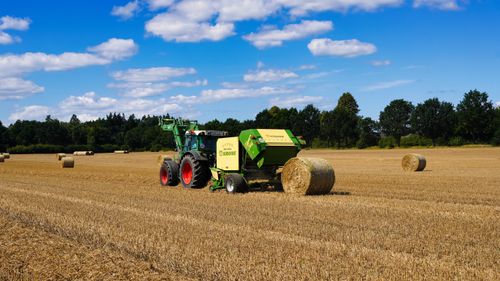 Free A tractor operates in a wheat field in Hohenhorn, harvesting hay bales on a sunny day. Stock Photo