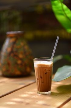 Refreshing iced coffee on a sunny outdoor table with greenery in the background.
