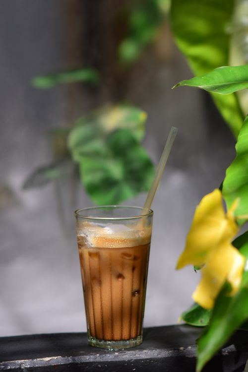 Free Tall glass of iced coffee with straw, surrounded by vibrant tropical leaves. Stock Photo