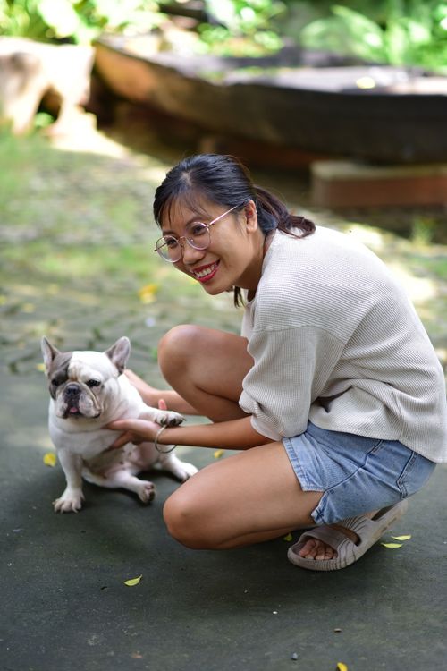 Free Woman kneeling with a French Bulldog in a sunny outdoor setting. Stock Photo