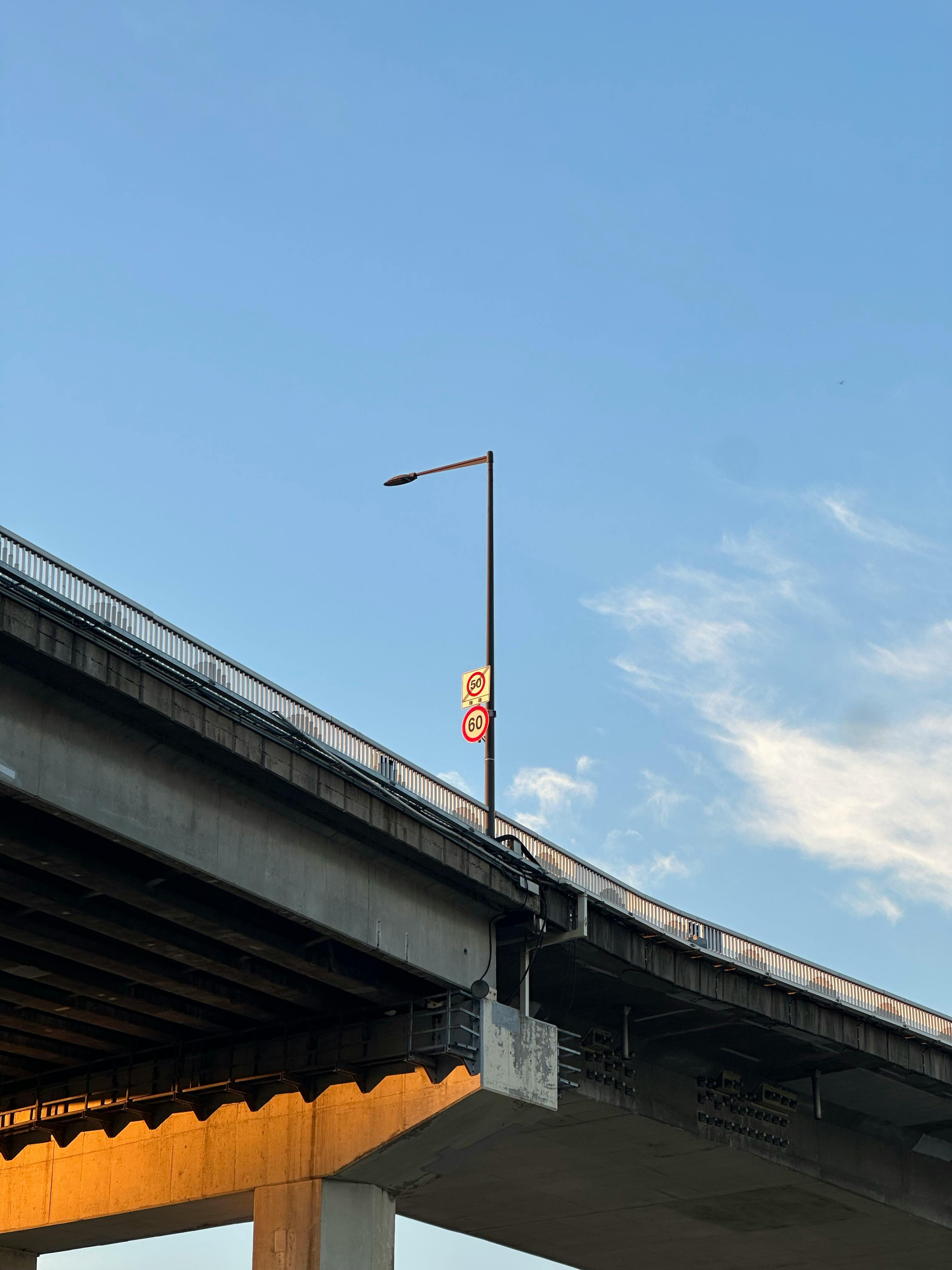 Concrete overpass with street light and traffic sign under a bright blue sky.