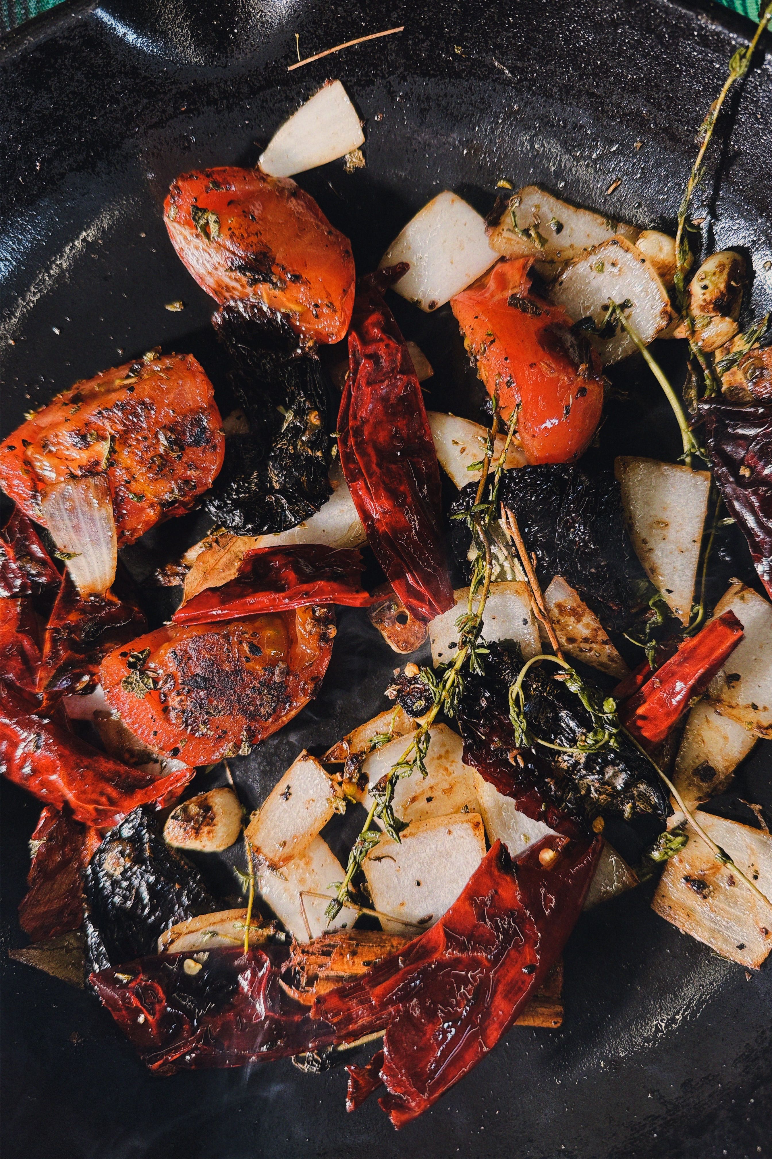 Surtido de vegetales asados incluyendo tomate y pimiento morrón en una sartén de hierro fundido.