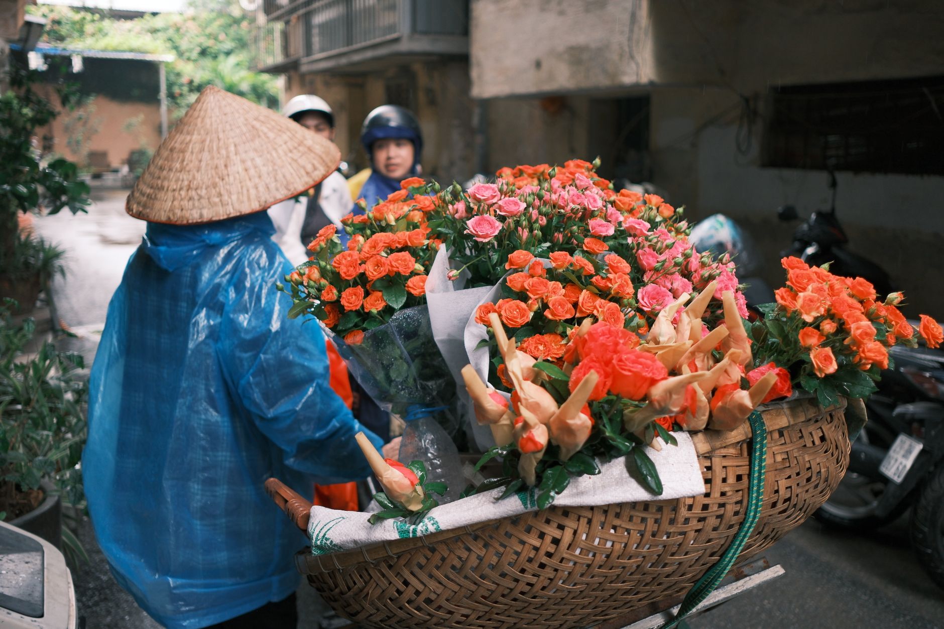 A street vendor in traditional attire sells a basket of vibrant flowers on a city street.