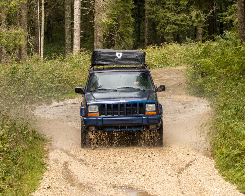 A rugged 4x4 vehicle navigates through muddy trails in the Asiago forests of Italy, showcasing adventure and nature.