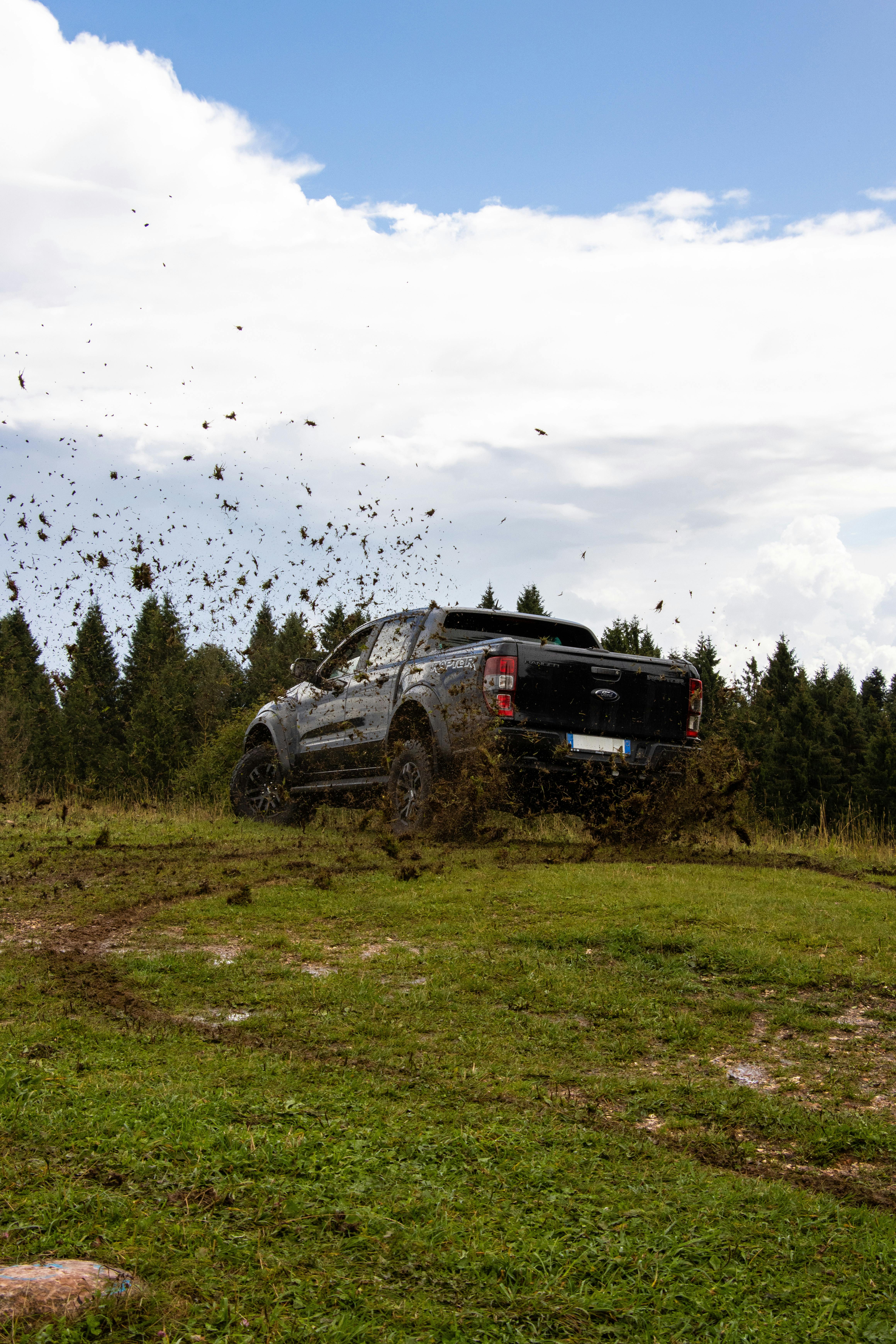 4x4 vehicle off-roading in Asiago, Italy, kicking up mud in lush forest setting.