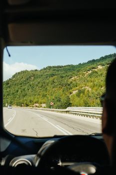View from car window of a scenic highway drive through lush green hills.