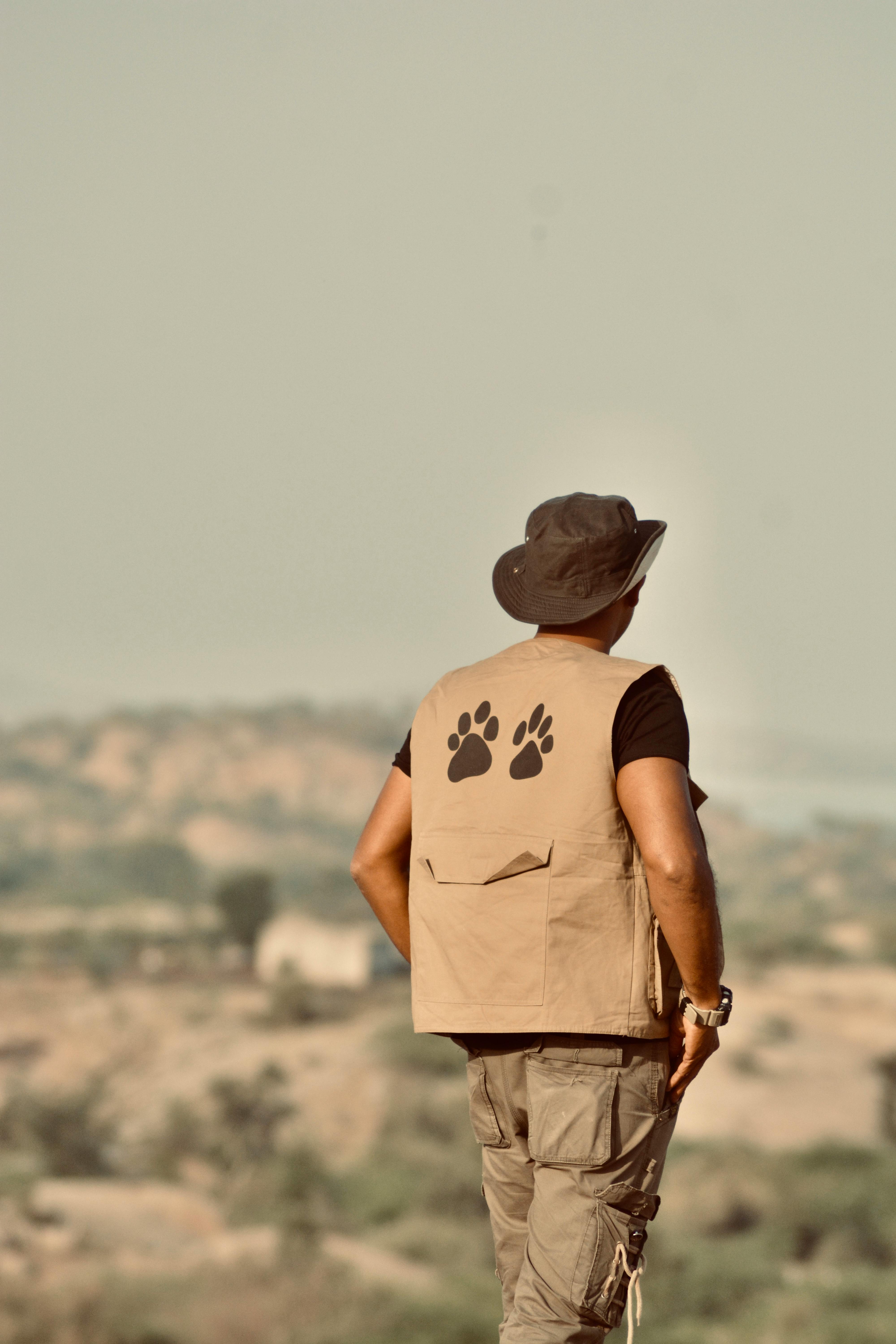 Gratuit Un bărbat cu o pălărie de safari și o vestă cu amprente de lăbuțe explorează un peisaj accidentat. Fotografie de stoc