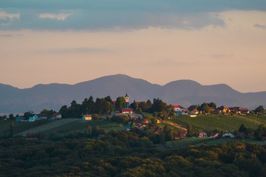 Beautiful village landscape at sunset with a church, vineyards, and mountains in the background.