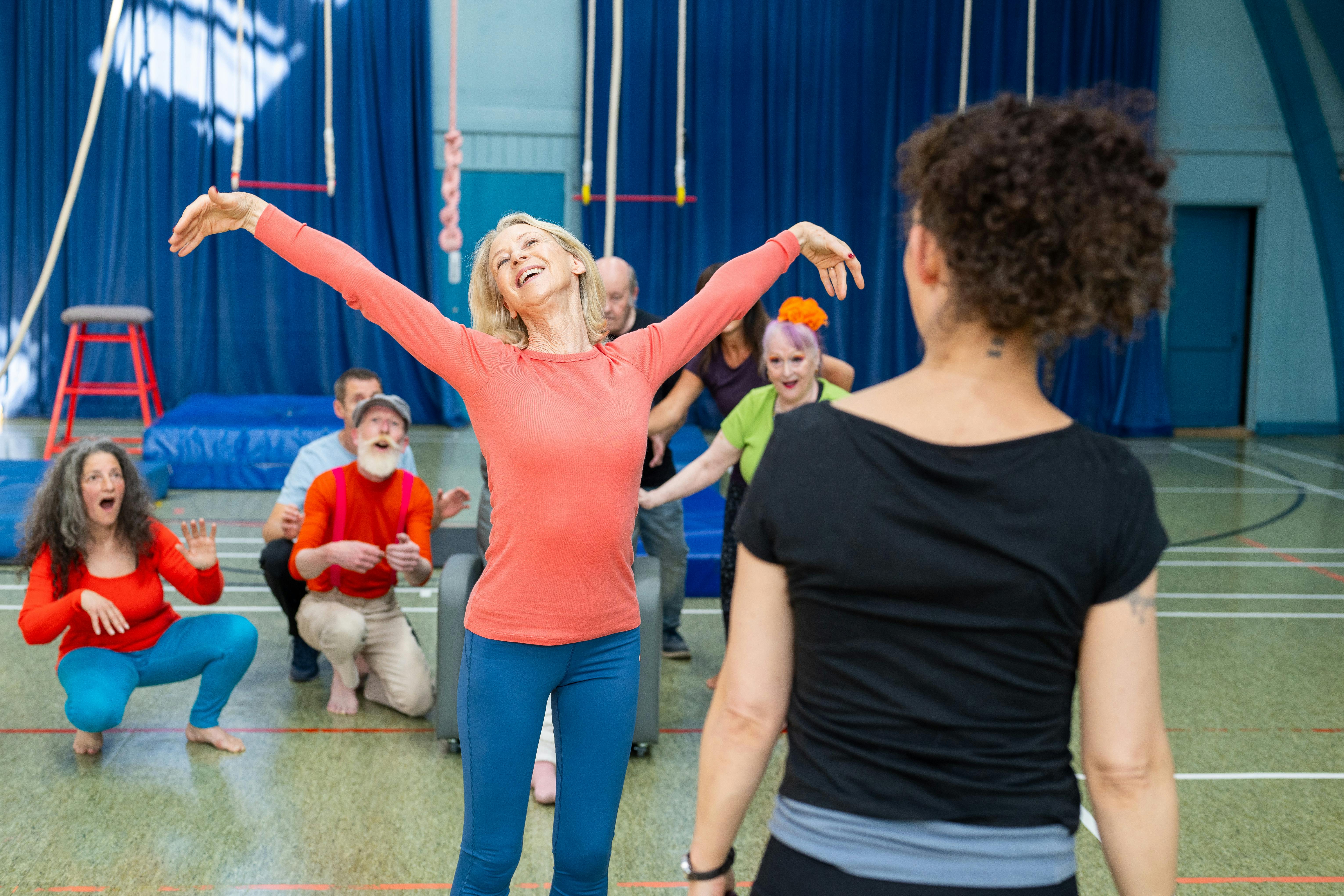 A group of enthusiastic adults participating in a lively circus workshop indoors, showcasing teamwork and joy.
