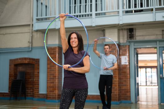 Two senior adults enjoying a hula hoop exercise class indoors with smiles.