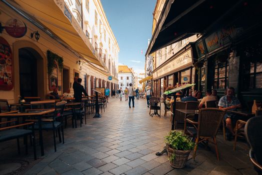 Lively café-lined street in Bratislava's historic city center under a clear sky. - Fotografer Sidoarjo
