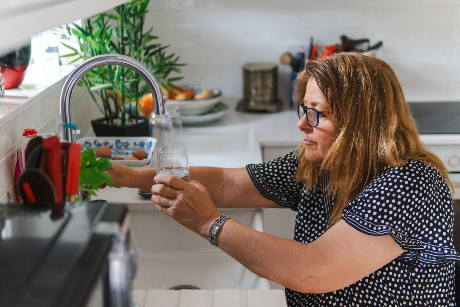 A woman filling a drinking glass at her kitchen tap, the fluid half of the fiber-and-water pairing that softens stool