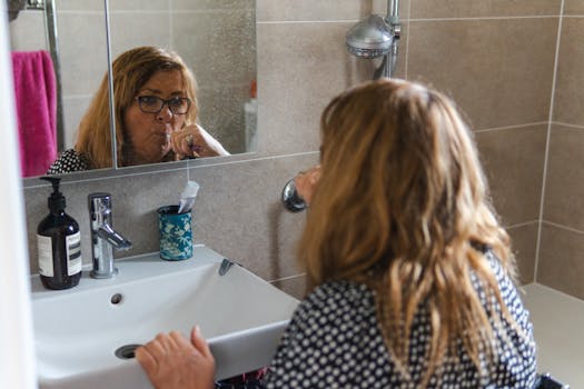 Adult woman brushing her teeth in the bathroom mirror, demonstrating daily hygiene routine.