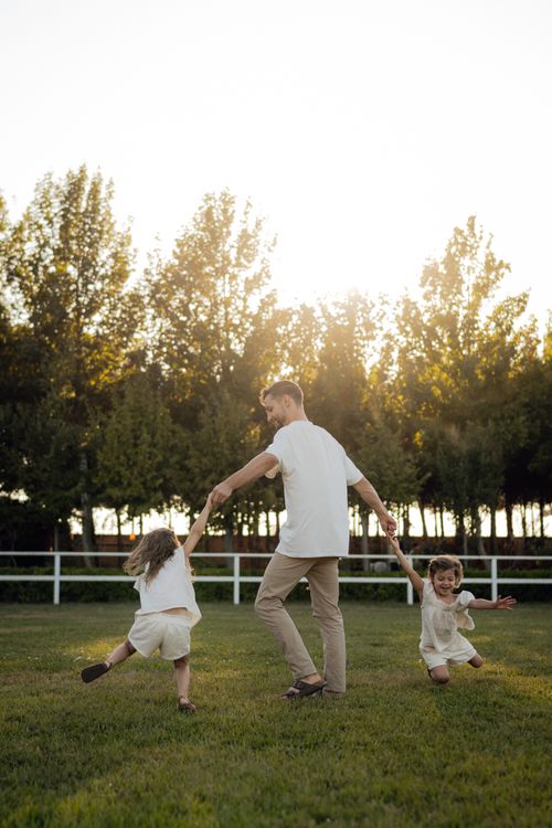 Free Father and daughters enjoying playful moments outdoors in a sunny park. Stock Photo