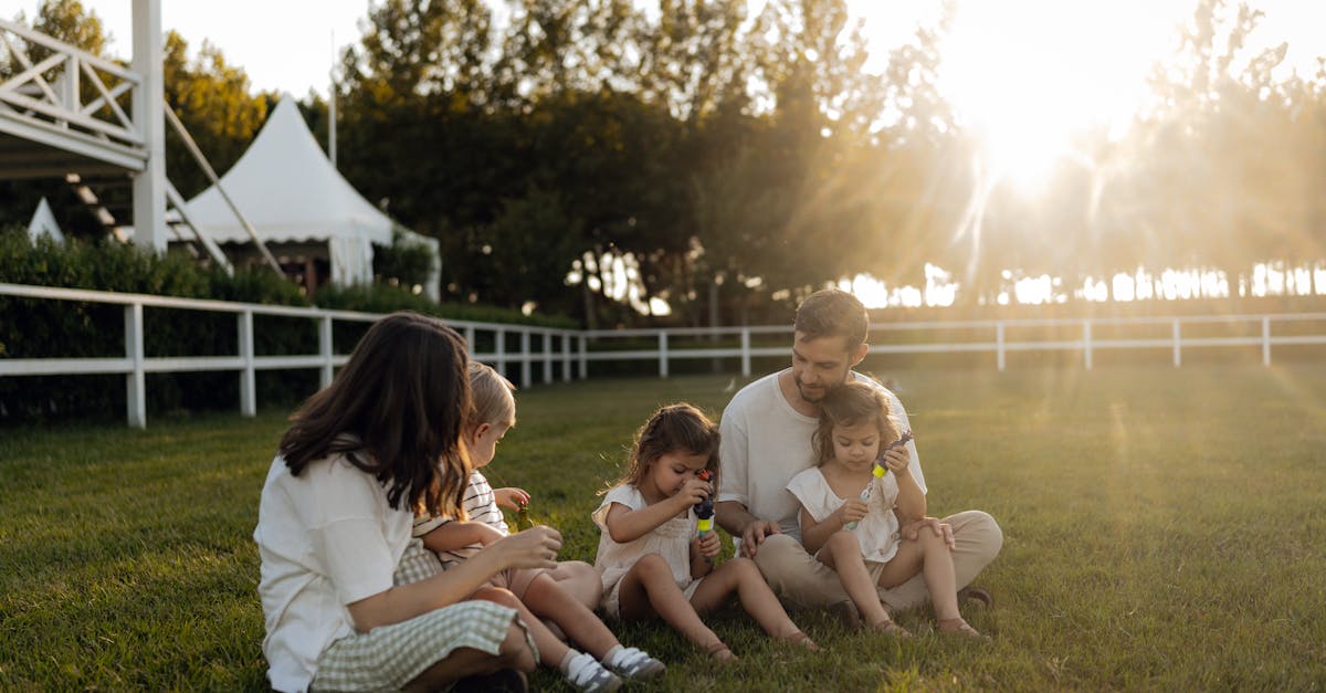 Family sitting on grass enjoying leisure time outdoors, with sun setting in the background.