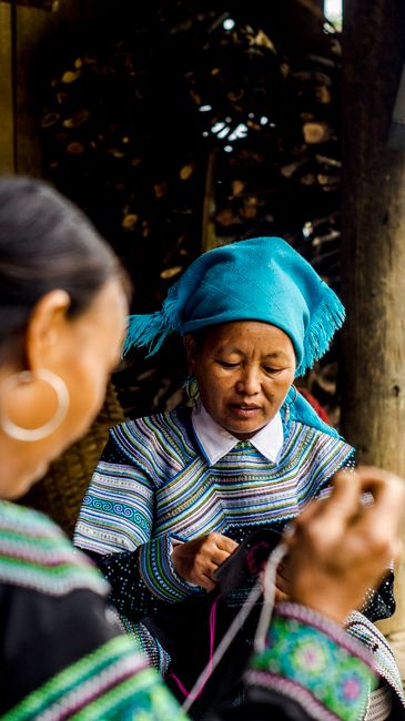 Two women knitting together, showcasing cultural attire and craftsmanship.