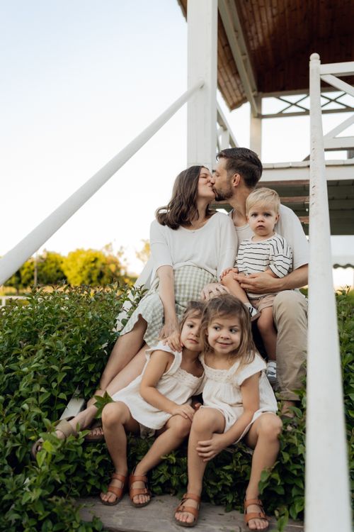 Free A joyful family of five sitting on steps outdoors, capturing a loving and serene moment in the sunshine. Stock Photo