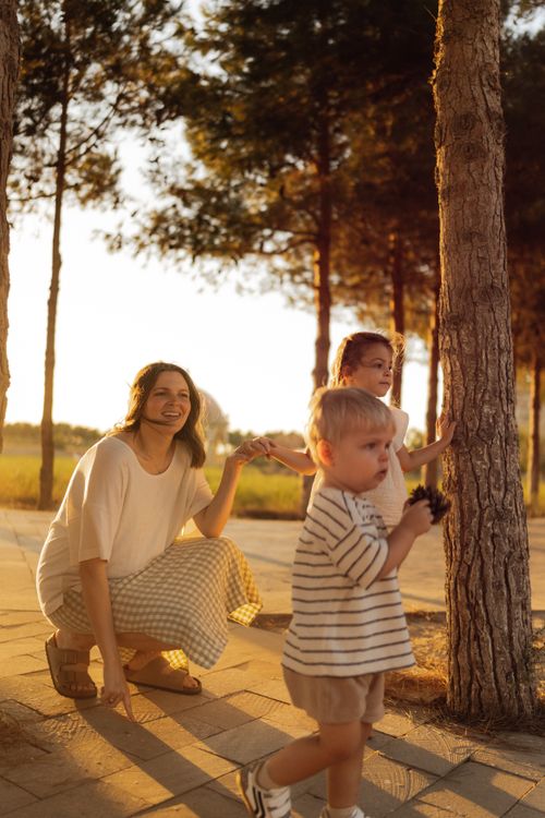 Free A mother and children enjoying a sunny day in the park, surrounded by trees. Stock Photo