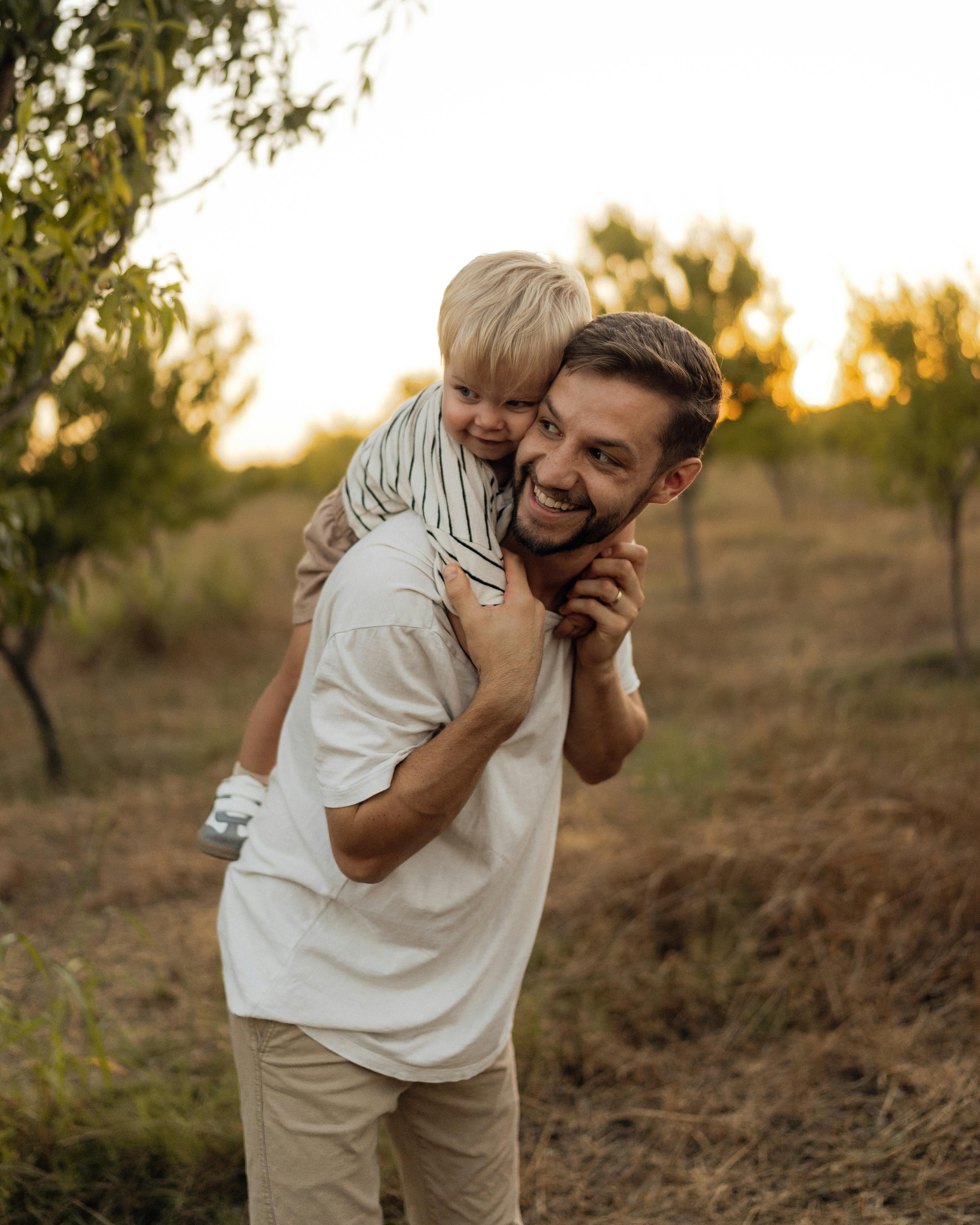 Heartwarming outdoor moment of a father piggybacking his son in a peaceful orchard setting at sunset.