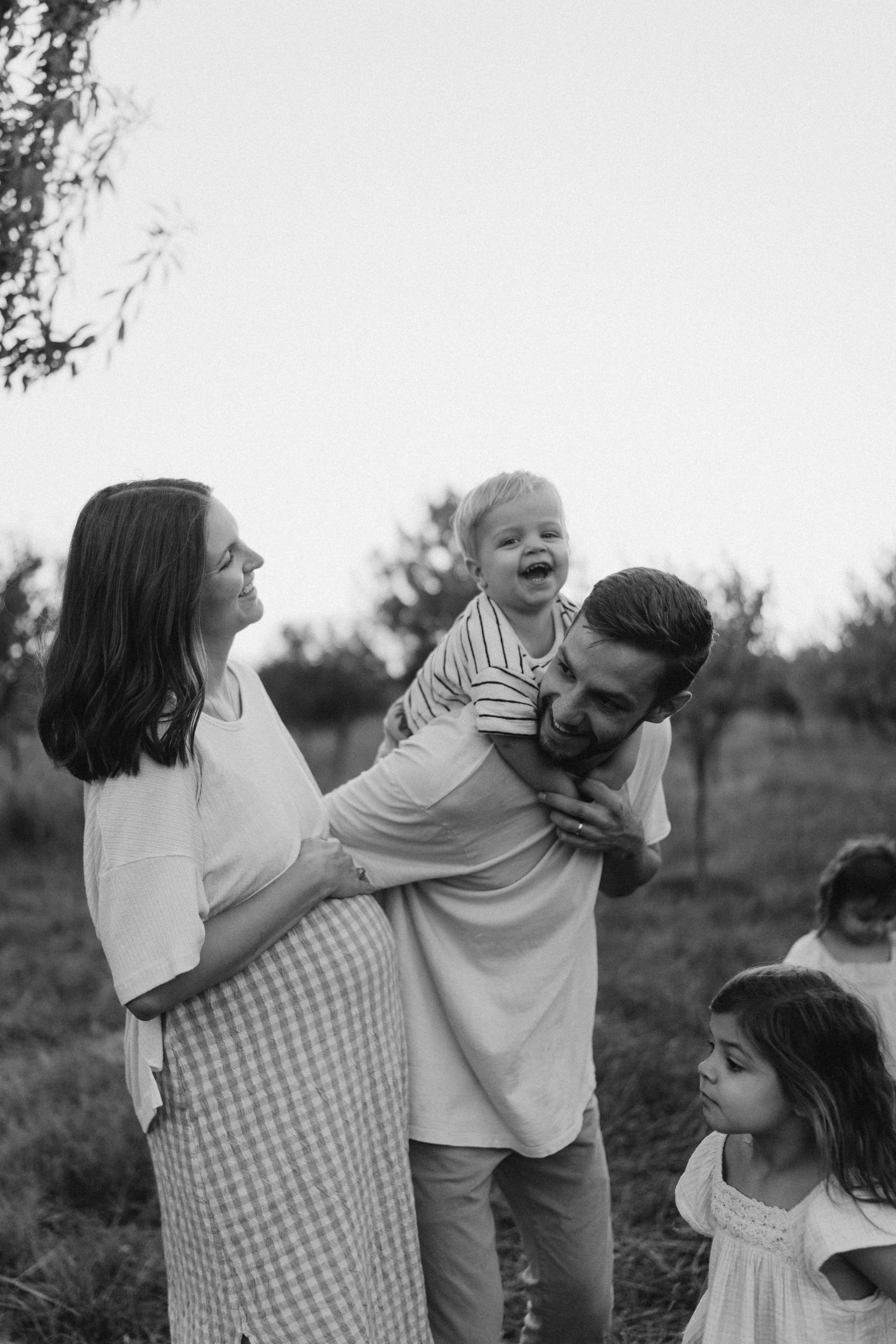 Candid black and white portrait of a family enjoying time outdoors in a natural setting.