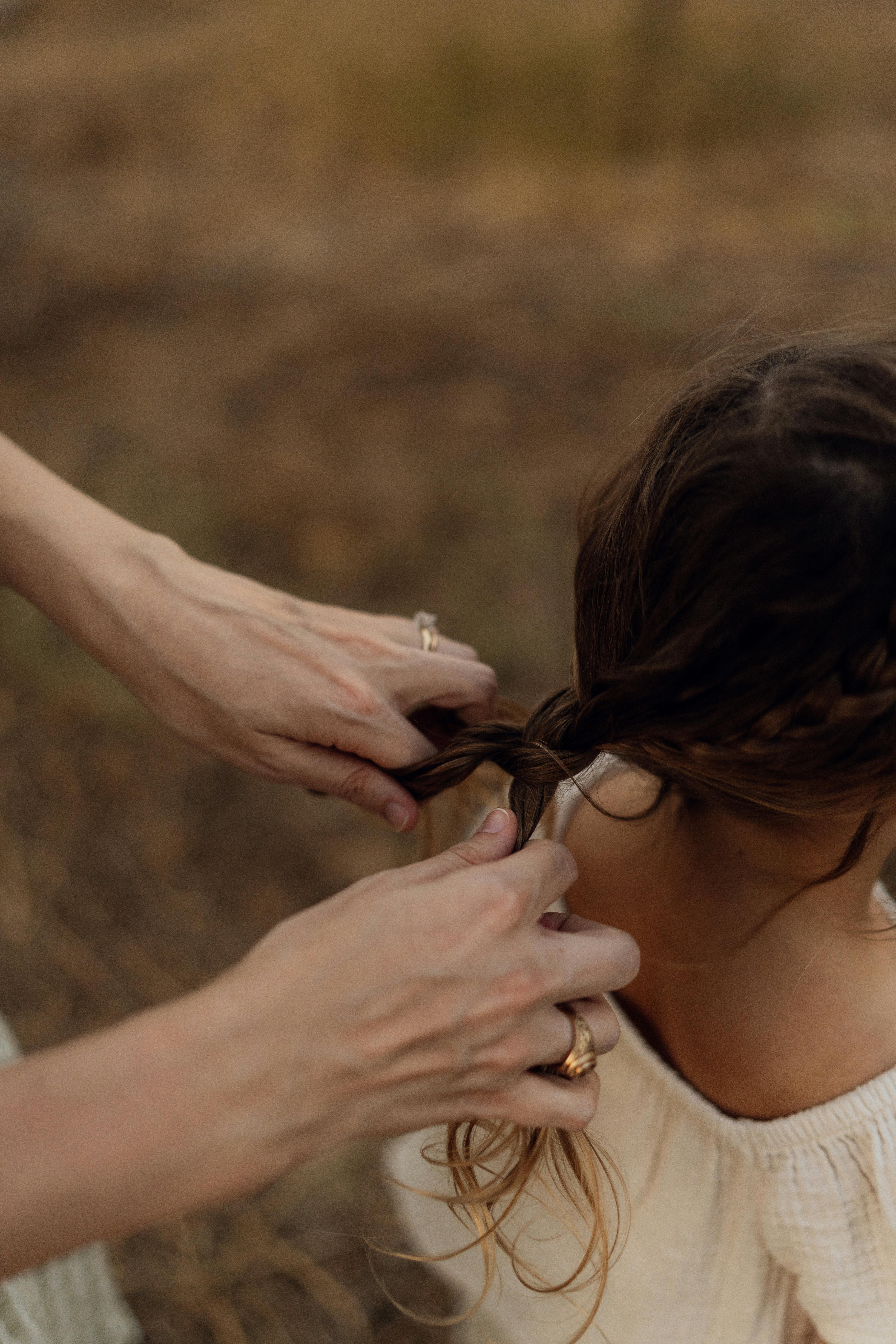 A woman gently braids a young girl's hair in an outdoor setting, showcasing a tender moment.