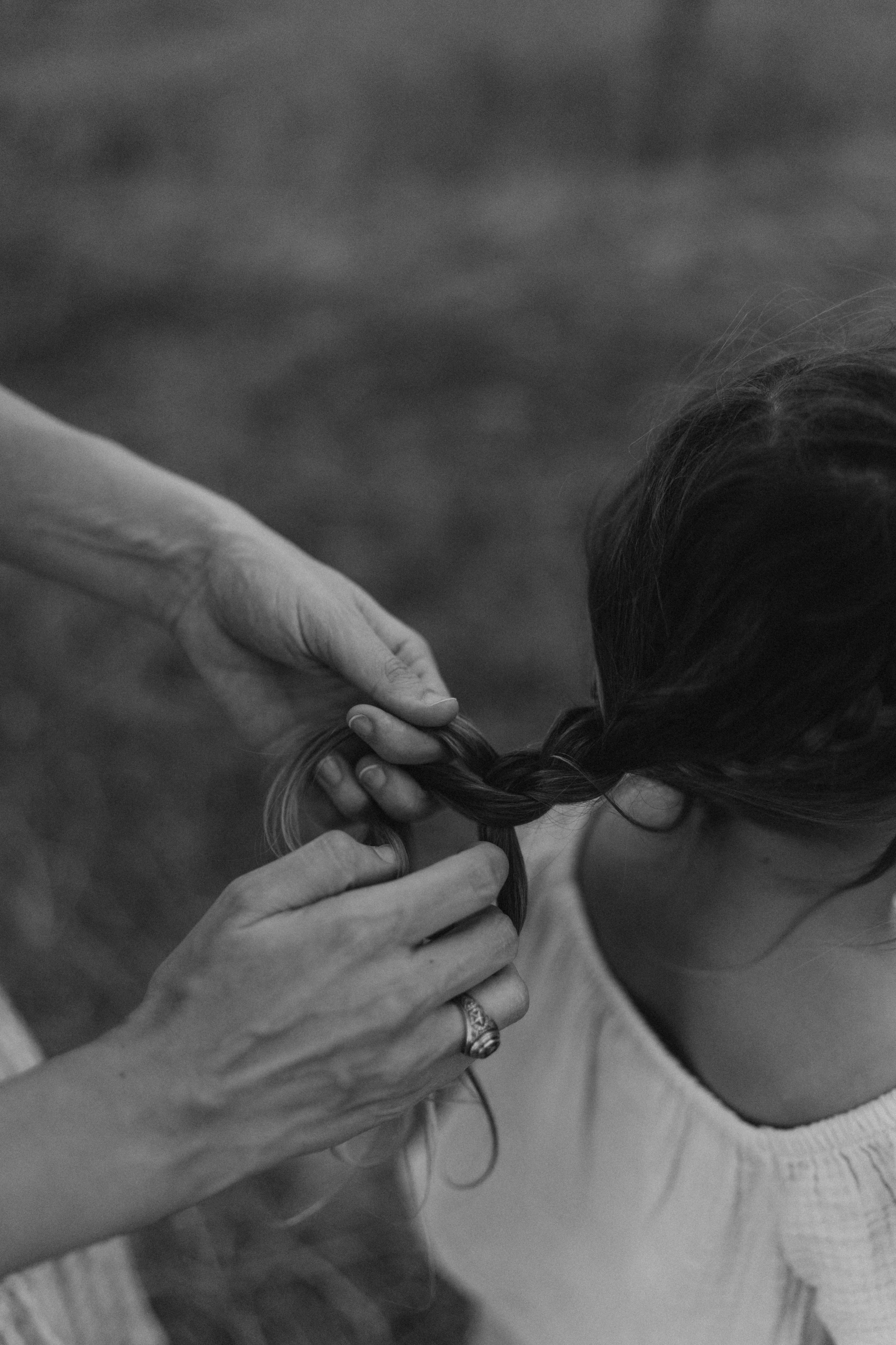 Monochrome image capturing the intimate moment of braiding hair outdoors.