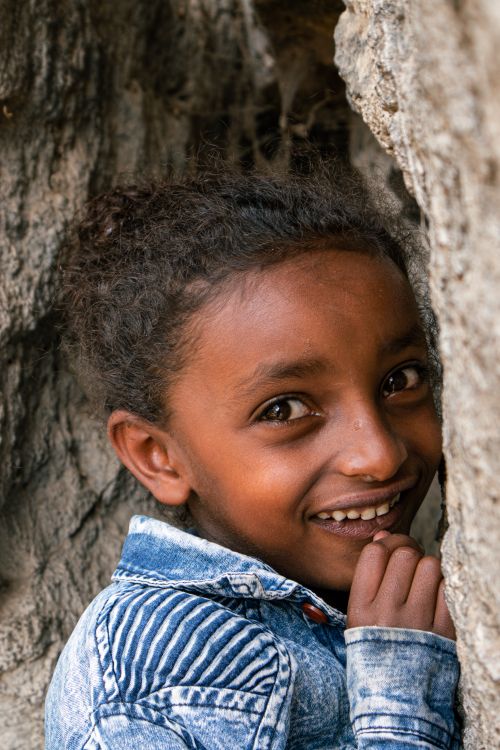 Free Young Ethiopian child smiling playfully against textured rocks. Stock Photo