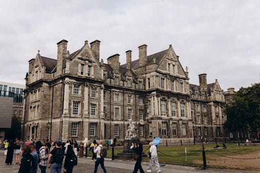 Historic architecture of Trinity College Dublin surrounded by visitors on a cloudy day.