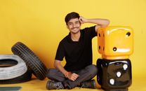 Smiling young man seated indoors with large dice and tires, exuding a positive and relaxed vibe.