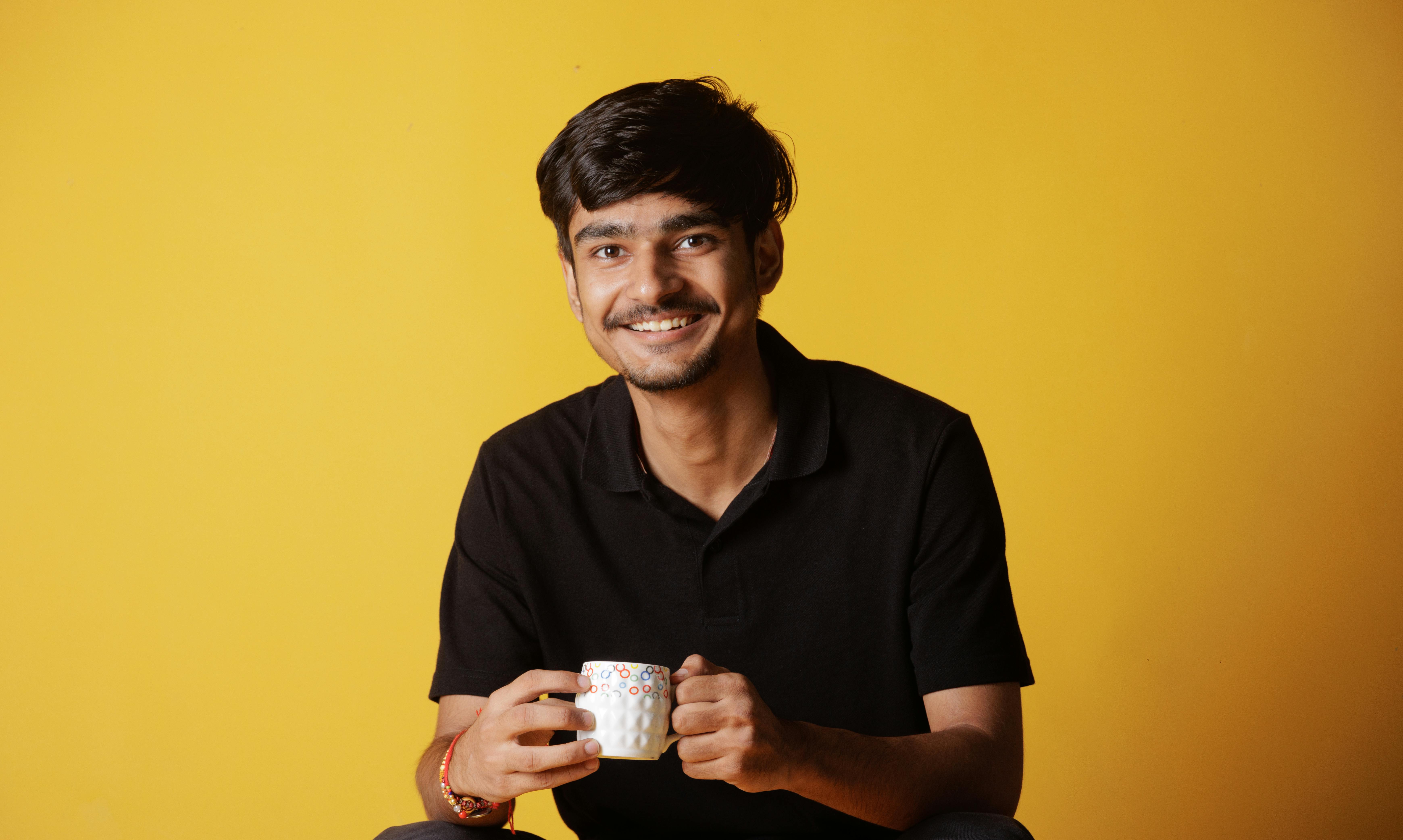 A cheerful young man enjoying a hot beverage indoors, exuding warmth and relaxation.