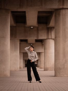 Confident woman posing amidst large concrete columns, embodying modern architectural elegance.