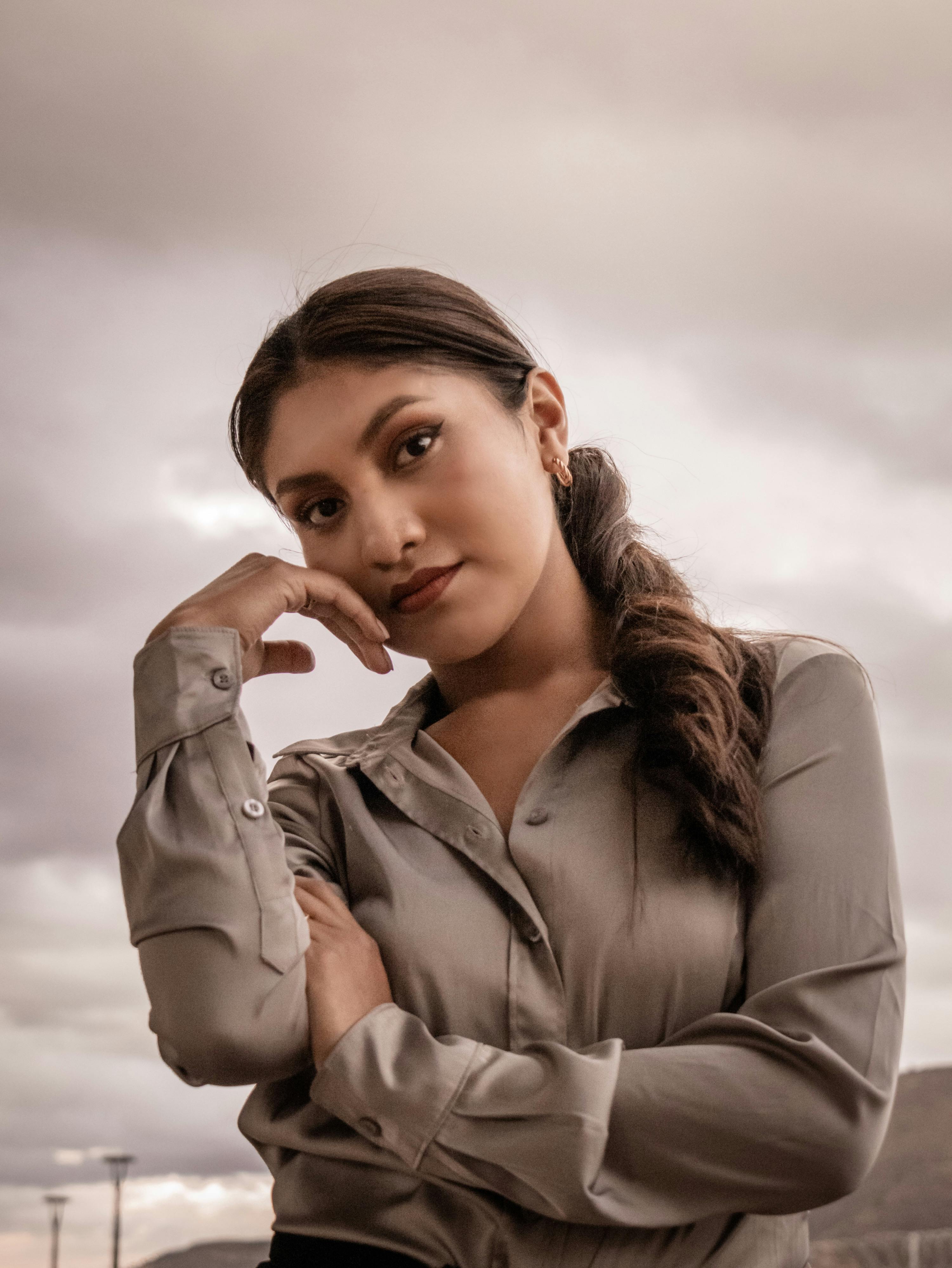 De franc Dona jove pensativa a l'aire lliure amb una expressió serena contra un cel malhumorat. Foto d'estoc