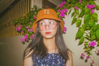 晚上，一位戴着水桶帽和眼镜的年轻女子站在鲜花丛中