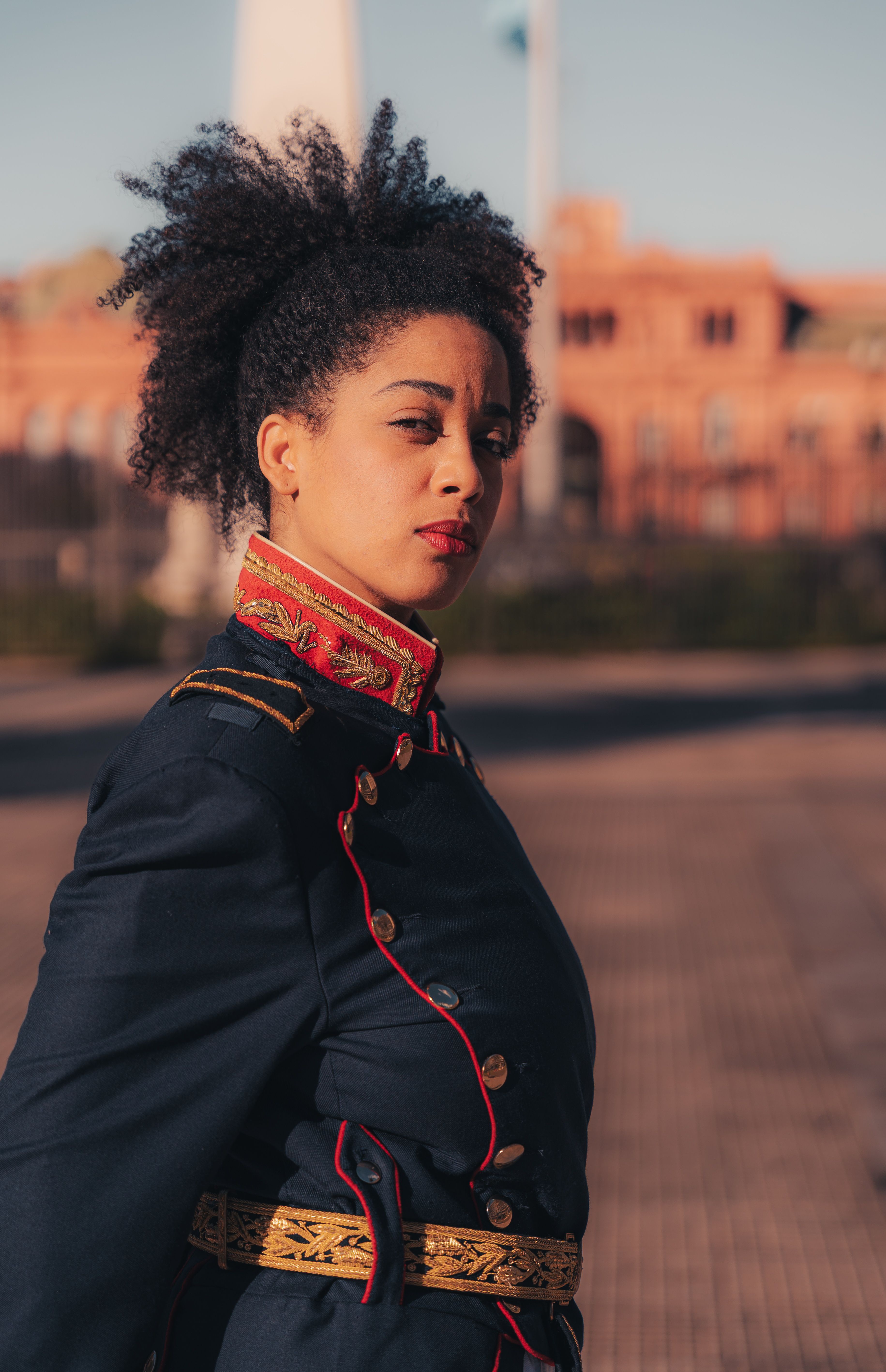 Portrait of a confident woman in traditional military uniform outdoors with a historic backdrop.