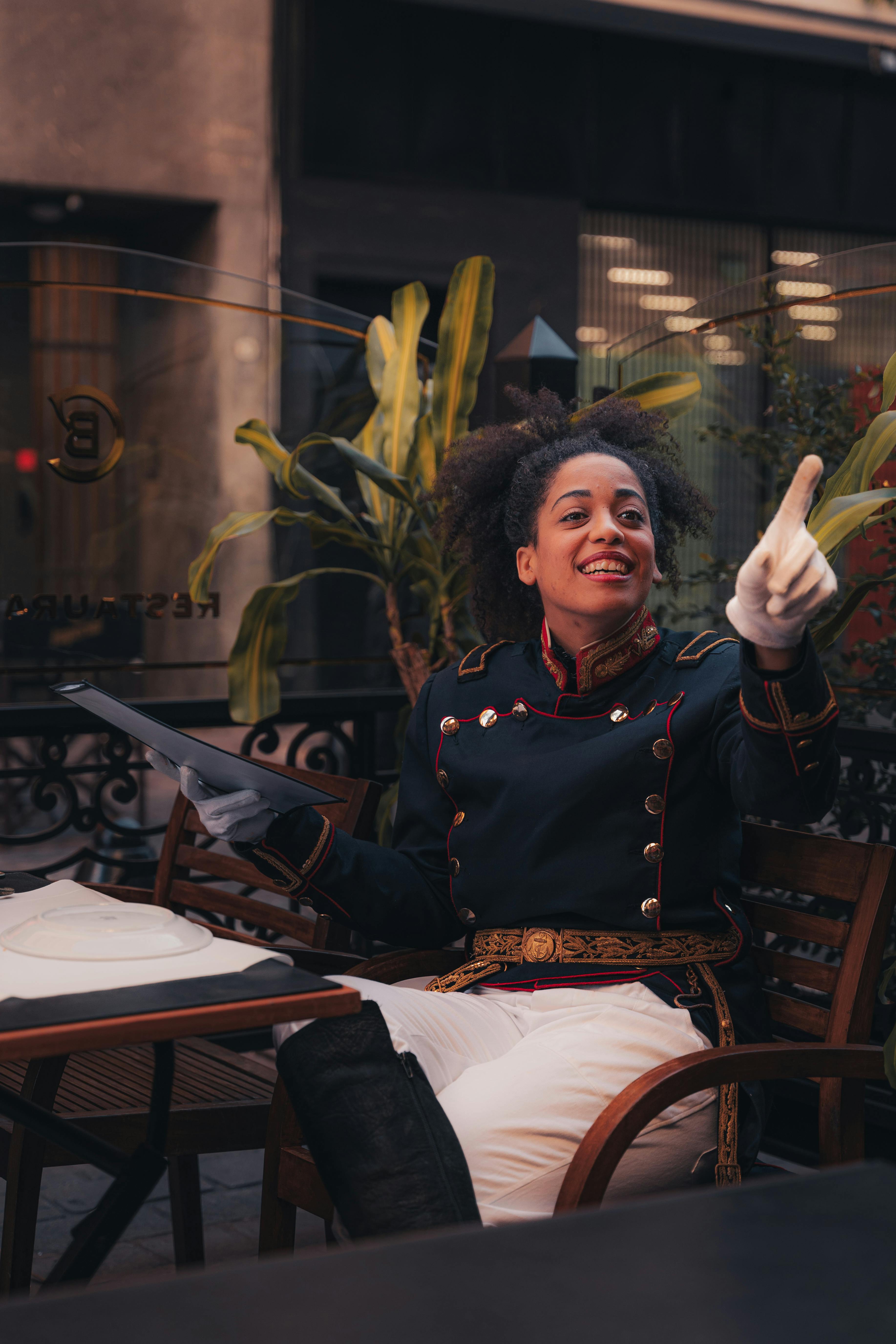 De franc Un cambrer alegre amb un uniforme històric dóna la benvinguda als clients en una acollidora cafeteria a l'aire lliure. Foto d'estoc