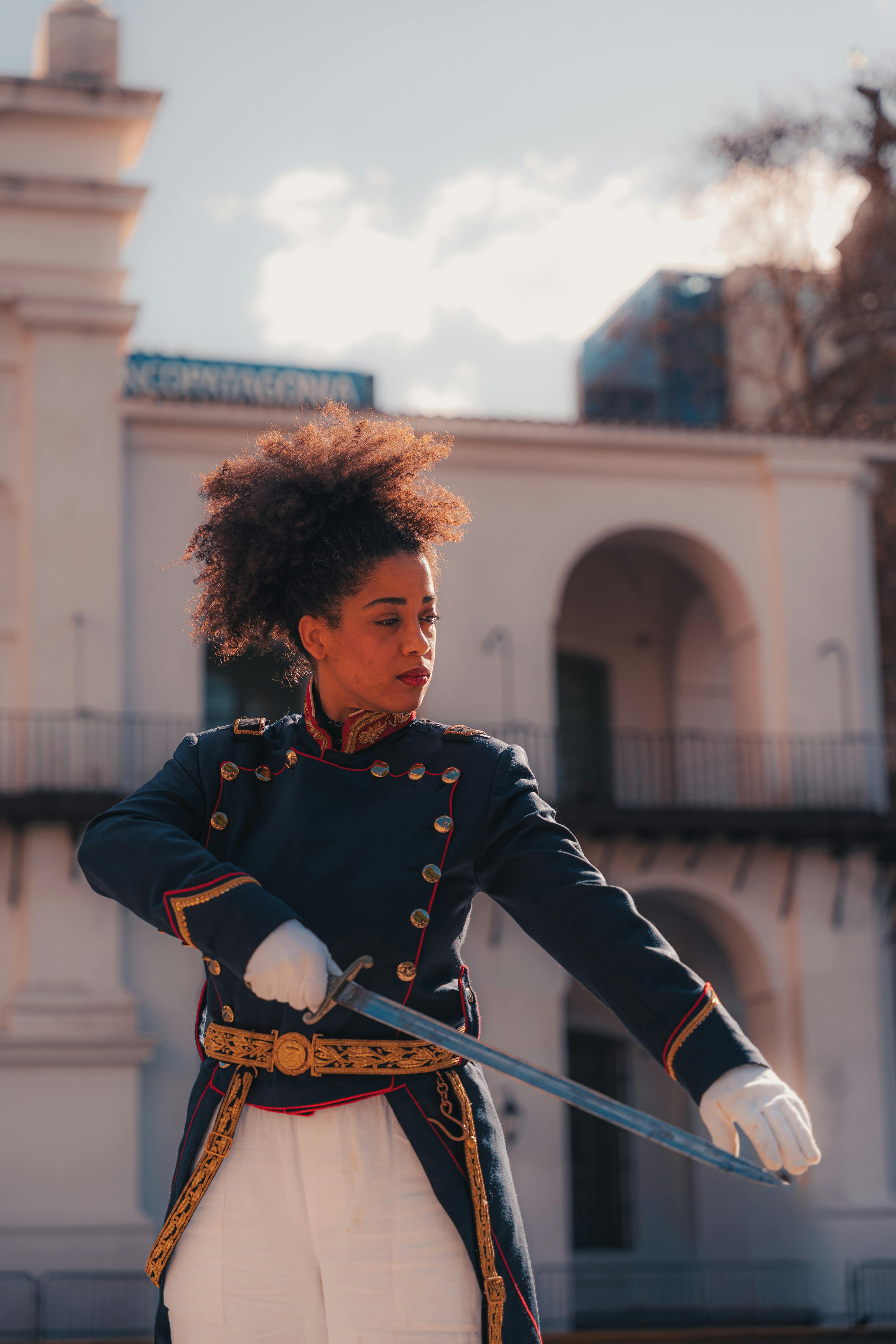 Swordswoman in historical military uniform performing in front of classical architecture.