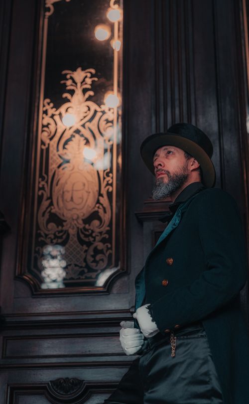 Free Portrait of a gentleman in vintage clothing leaning against an ornate door indoors. Stock Photo